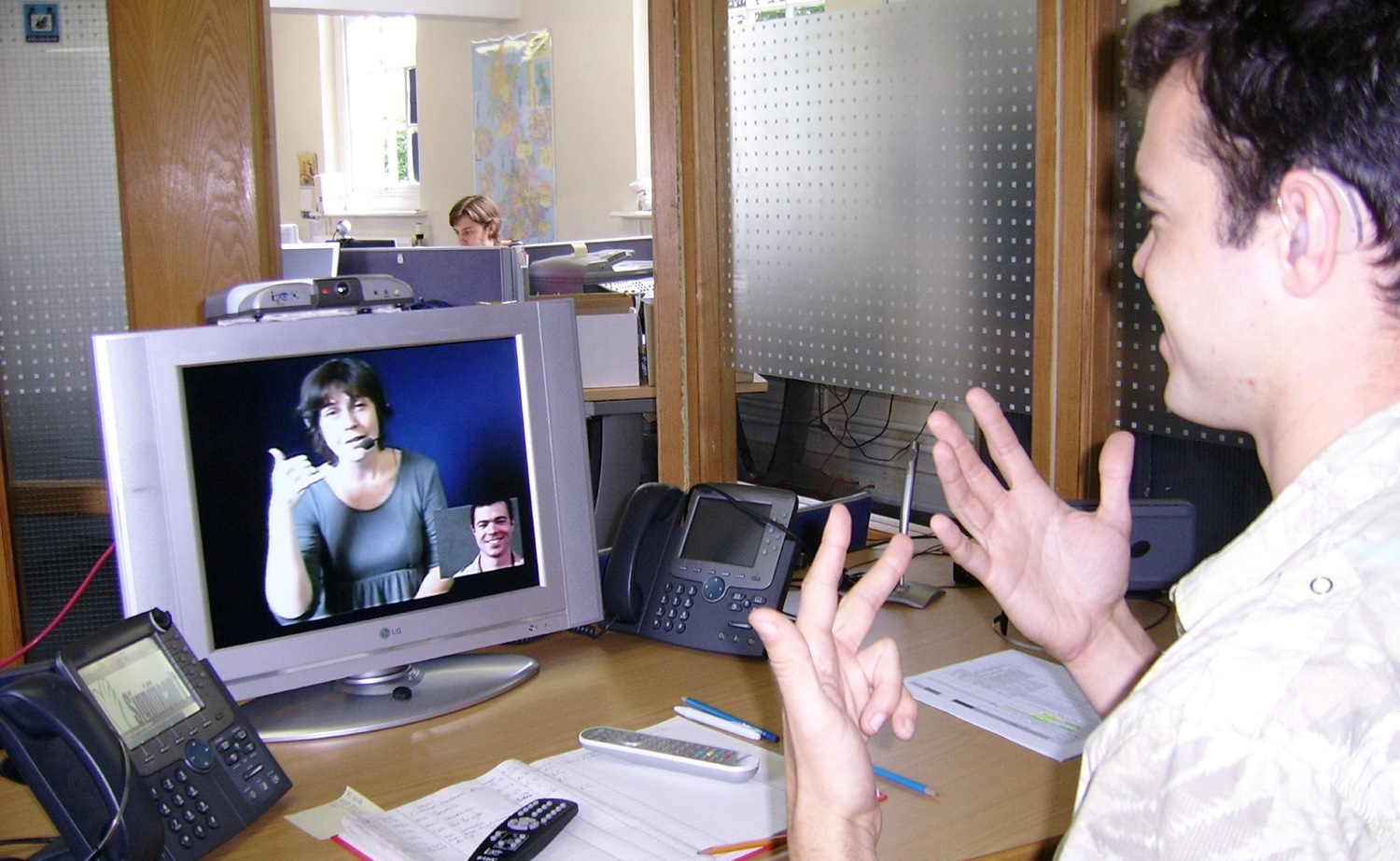 Deaf or HoH person at his workplace using a Video Relay Service to communicate with a hearing person via a Video Interpreter and sign language SVCC 2007 Brigitte SLI Mark